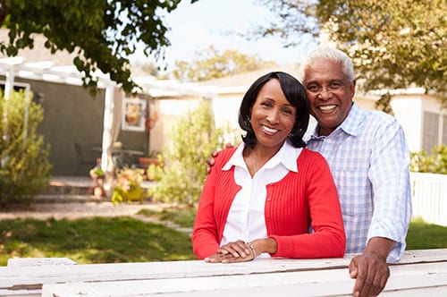 Senior Black Couple Look To Camera Outside Their New House.jpg